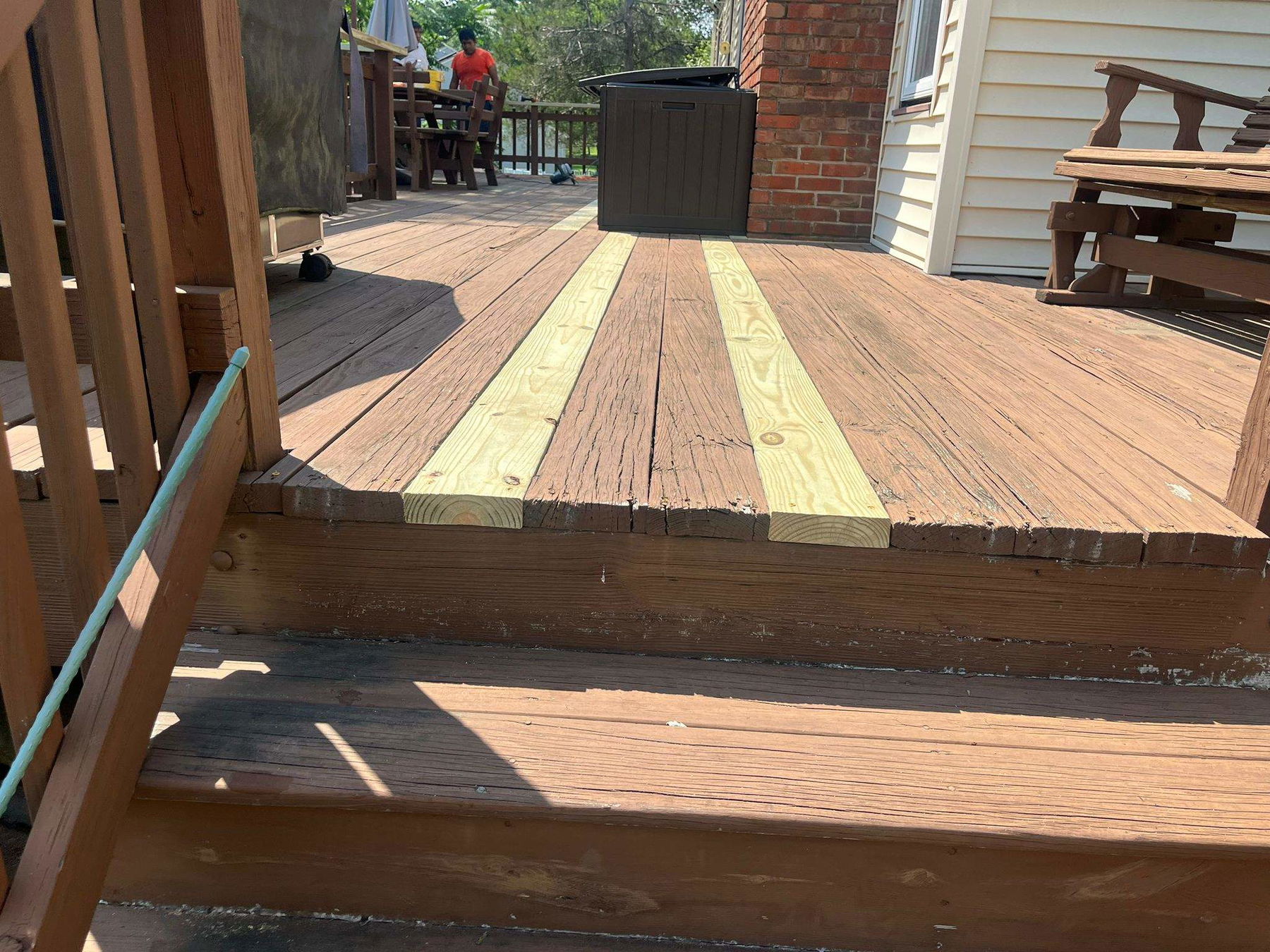 Multi-level deck in Bridgewater with mixed-stain wood decking featuring light yellow accent boards, wooden railings, and brick house exterior in background.