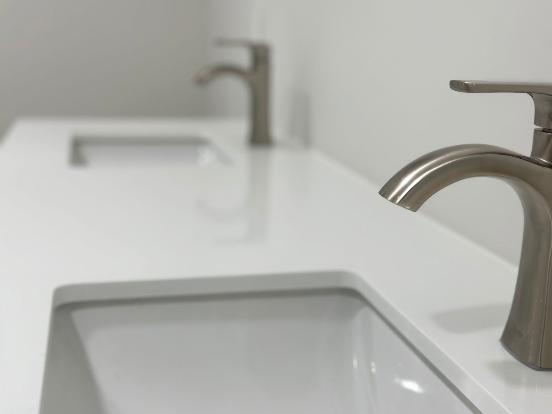 White rectangular vessel sink with brushed nickel arc faucet and matching single-handle bathroom fixtures on white countertop.