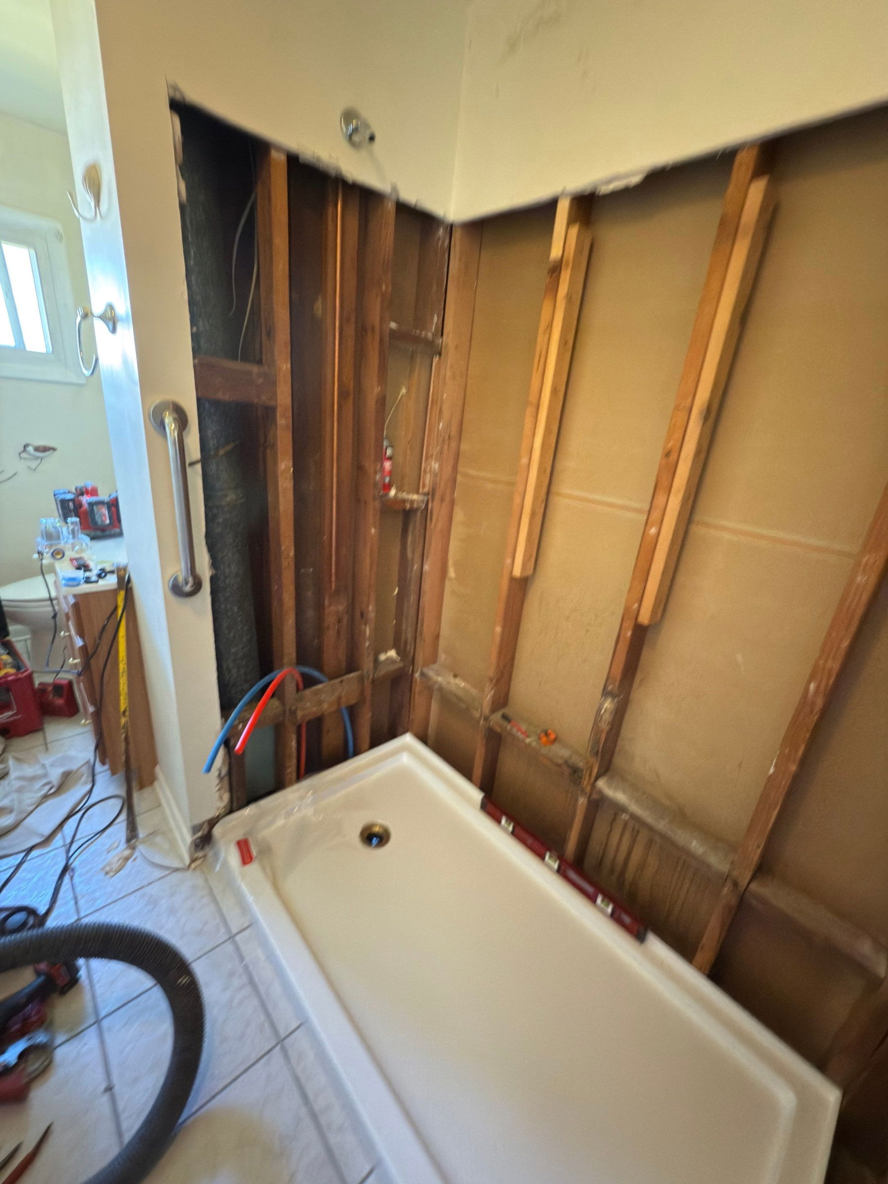 Bathroom under renovation with white soaking tub, wood-framed shower enclosure with glass doors, tan walls, and construction materials visible.
