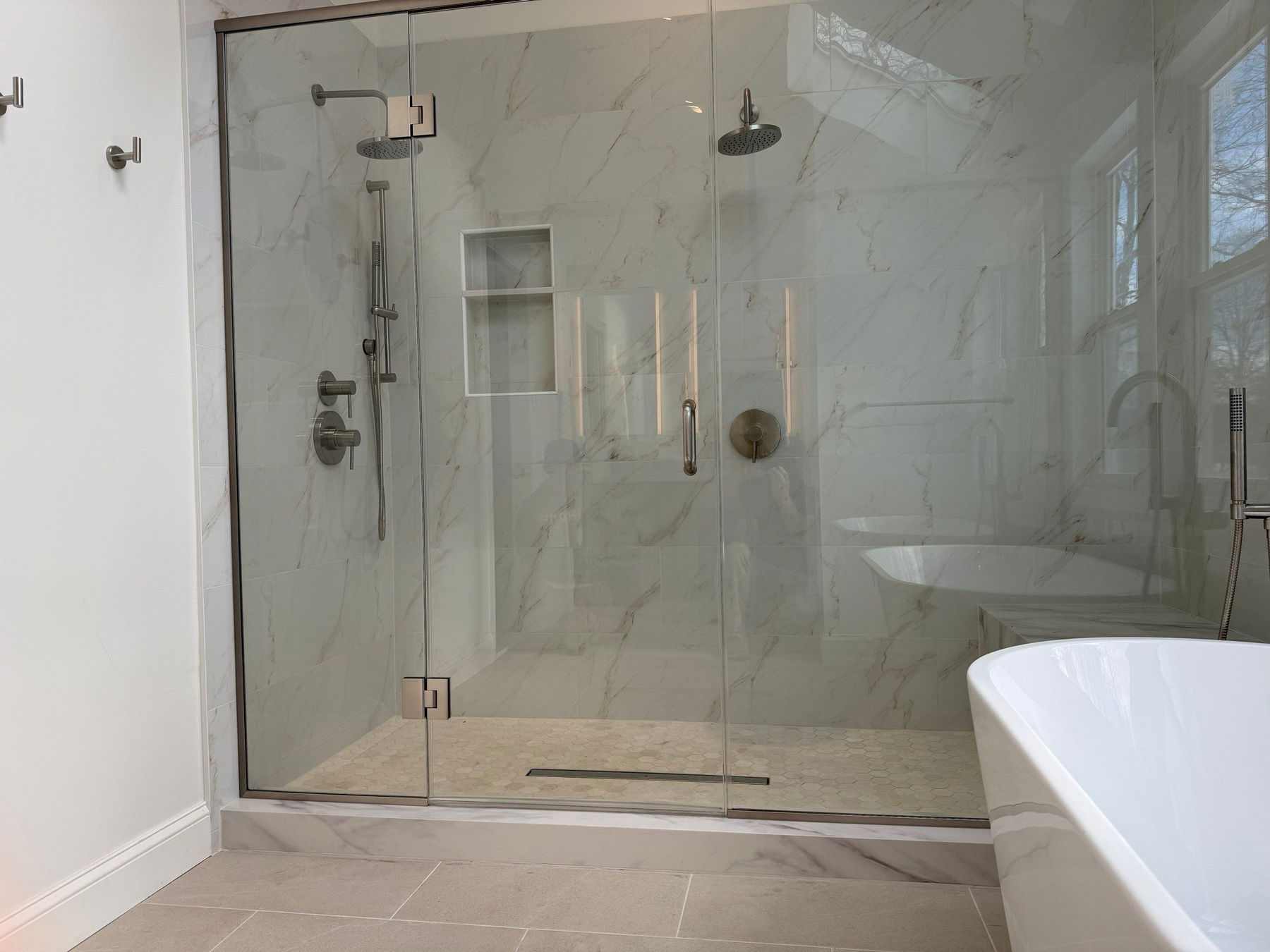 Warren master bathroom remodel featuring a large walk-in shower with marble-look porcelain tile walls, dual rainfall showerheads, brushed nickel fixtures, recessed niche, and a freestanding white soaking tub.