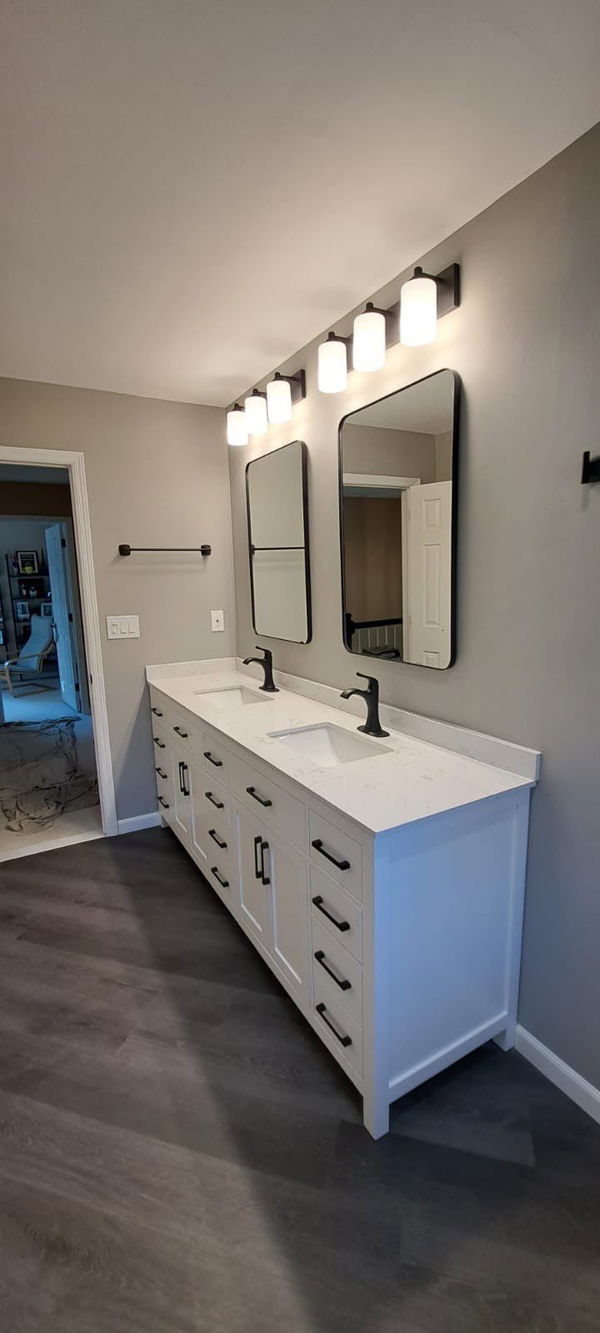 Dual-sink bathroom vanity with white cabinetry, quartz countertop, black faucets, framed mirrors, and five-light vanity fixture above dark tile flooring.