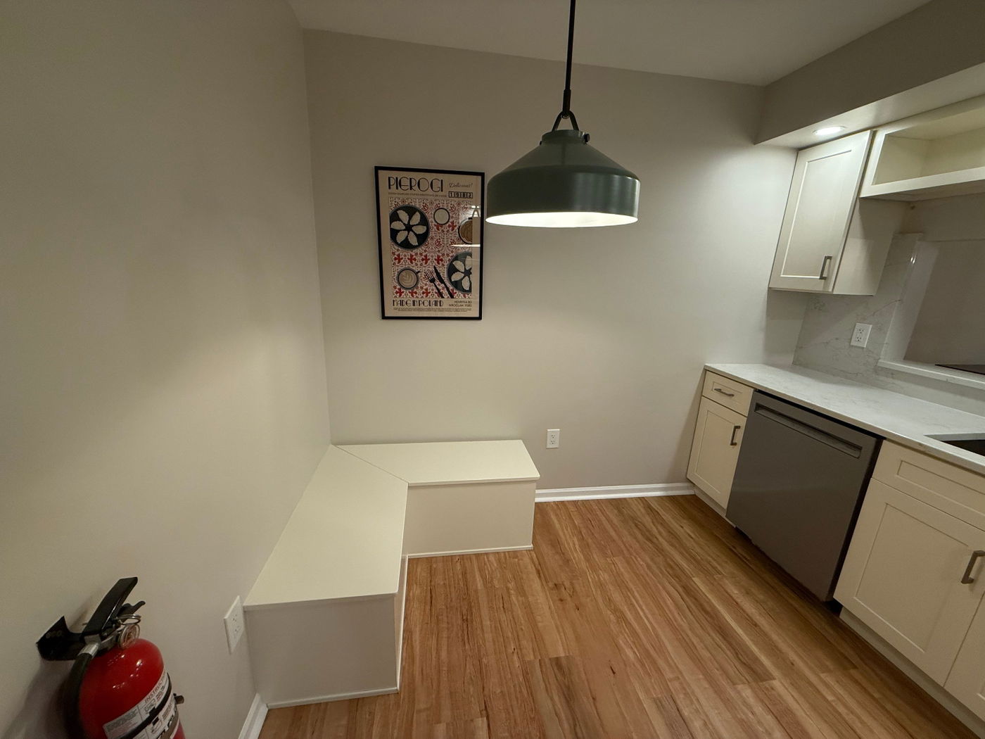 Modern kitchen with light wood cabinetry, white quartz countertops, wood-look flooring, pendant lighting, and stainless steel appliances.