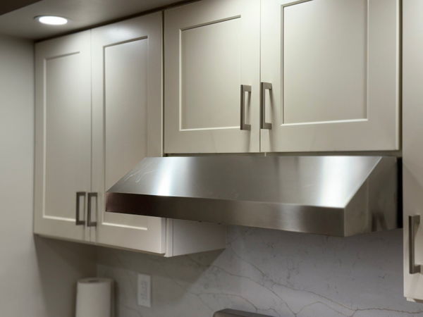 Modern bathroom vanity with white framed cabinetry, brushed nickel hardware, stainless steel vessel sink, and light marble backsplash.