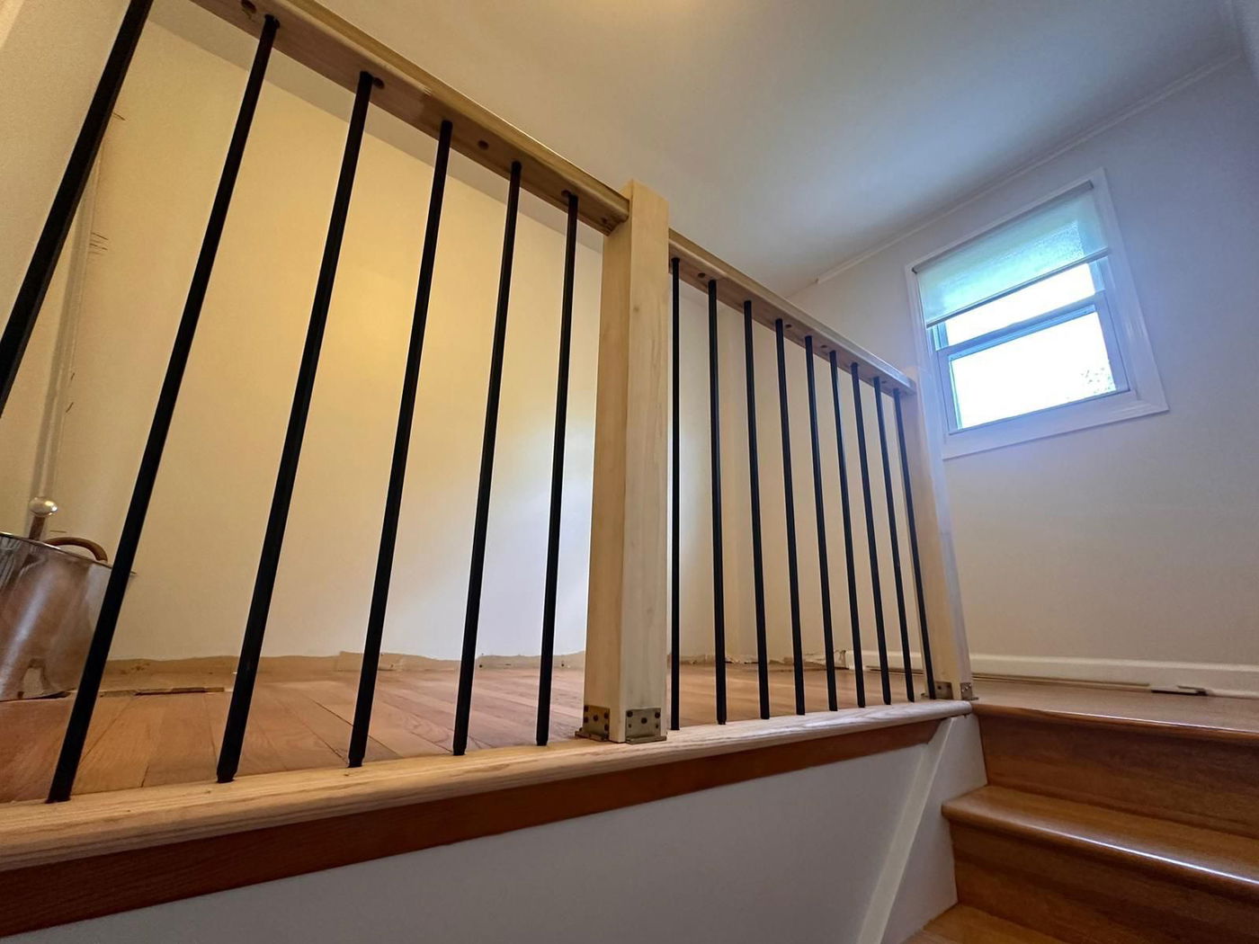 Denville interior renovation featuring a staircase with black metal balusters, natural wood handrail, and light-filled landing with transom window overlooking hardwood flooring.