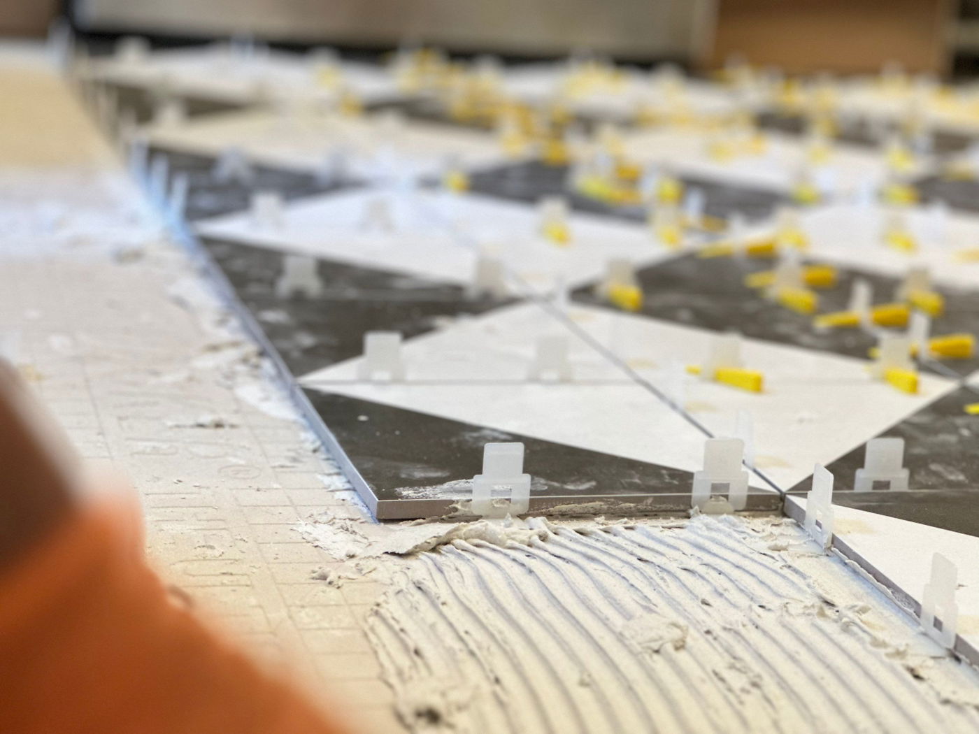 Kitchen Remodeling in Montclair, NJ — Home Concepts Construction Tile installation with white spacers and thinset mortar on subfloor, showing mixed black and white rectangular tiles with yellow markings.