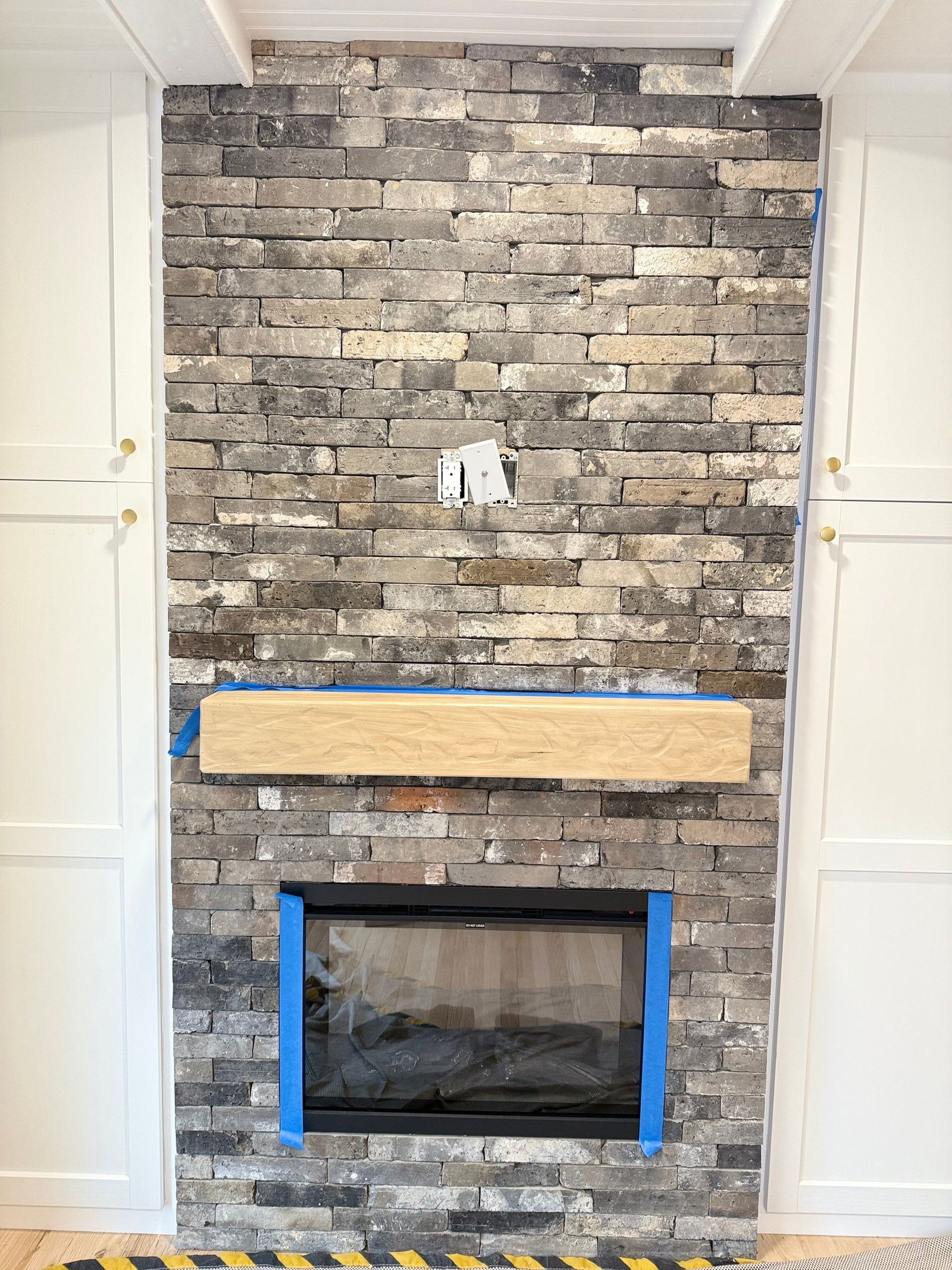 Morris Plains master bedroom fireplace with mixed-tone stacked stone veneer, black firebox insert, and wood mantel shelf framed by white trim and brass hardware.