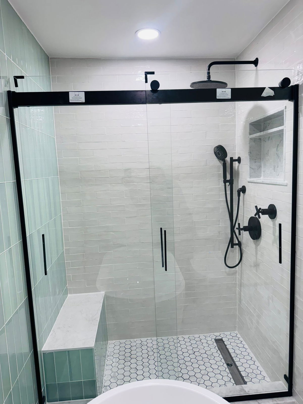 Morristown bathroom remodel featuring a walk-in shower with black-framed glass enclosure, white subway tile walls, hexagonal mosaic floor, black plumbing fixtures, and rainfall showerhead.