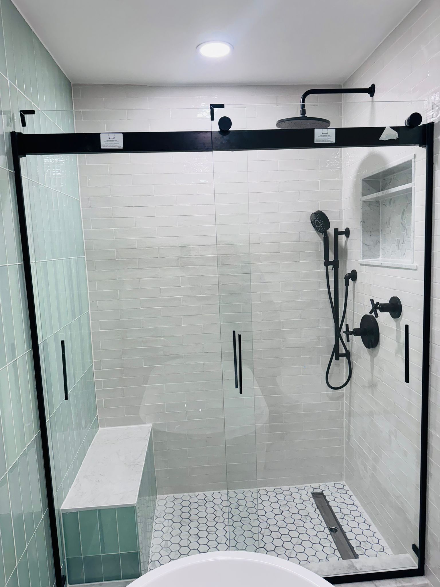 Morristown bathroom remodel featuring a walk-in shower with black-framed glass enclosure, white subway tile walls, hexagonal mosaic floor, black plumbing fixtures, and rainfall showerhead.