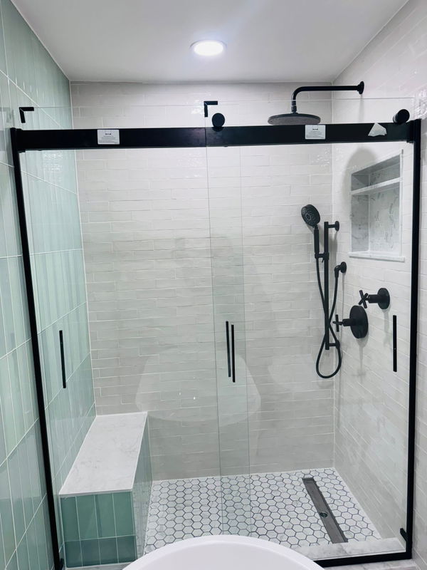 Morristown bathroom remodel featuring a walk-in shower with black-framed glass enclosure, white subway tile walls, hexagonal mosaic floor, black plumbing fixtures, and rainfall showerhead.