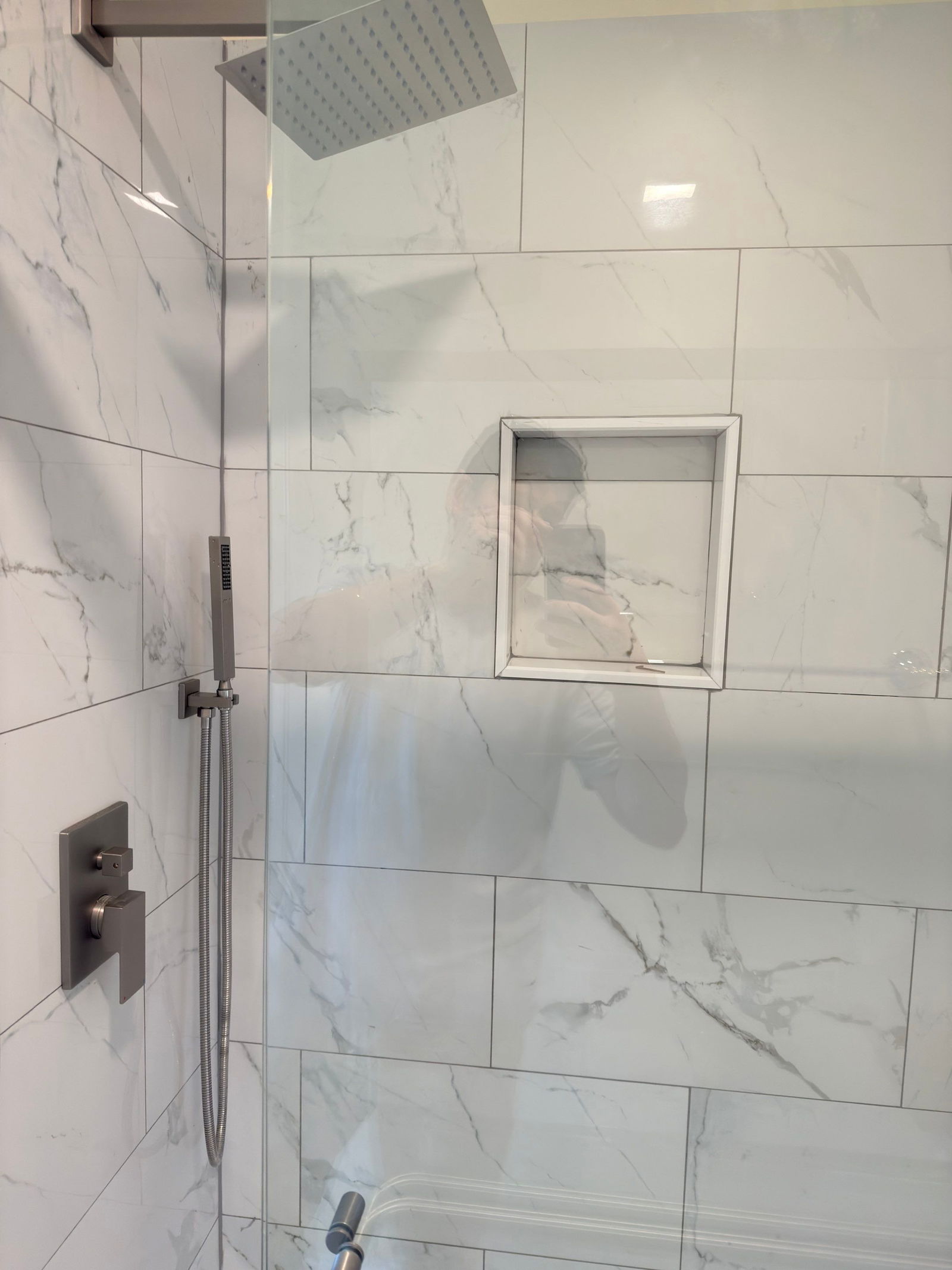 Walk-in shower with large-format marble-look tile walls, glass enclosure, built-in niche, and rainfall showerhead with matte black fixtures.