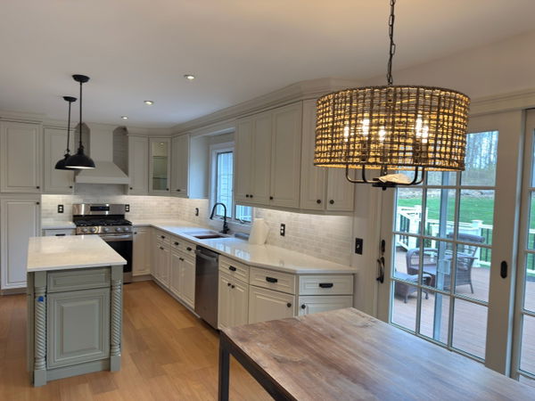 Open-concept kitchen with cream-colored shaker cabinets, white subway tile backsplash, stainless steel appliances, quartz countertops, woven pendant light, and French doors opening to a deck with green lawn views.