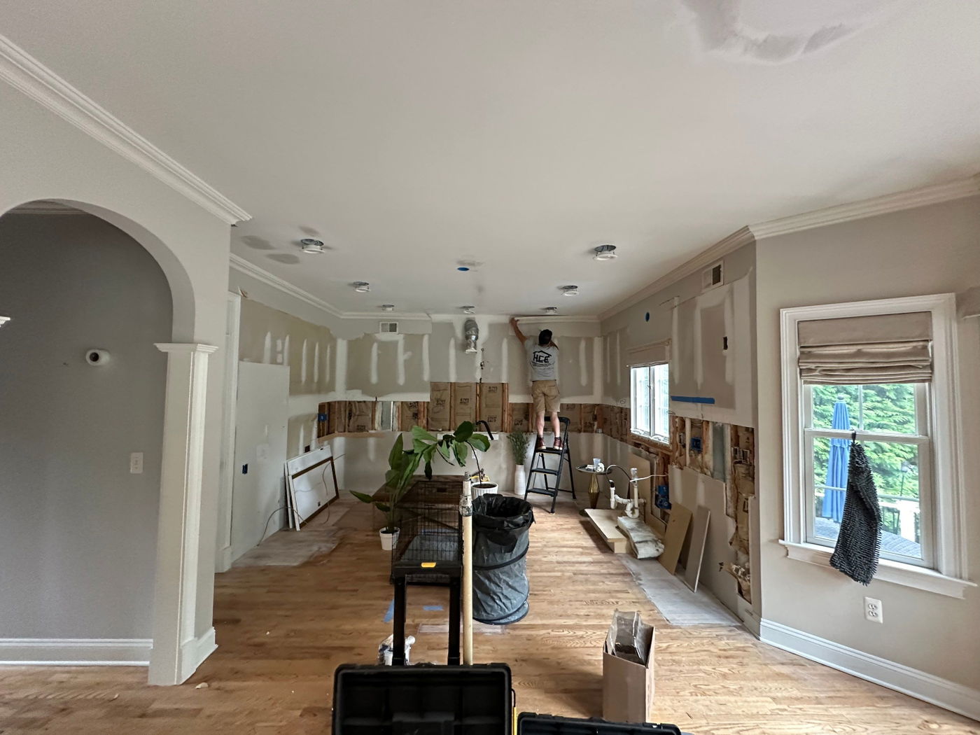 Open kitchen renovation in progress with white drywall, wood subfloor, recessed lighting, arched doorway, and large window with natural light.