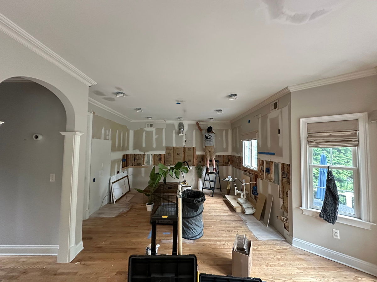 Open kitchen renovation in progress with white drywall, wood subfloor, recessed lighting, arched doorway, and large window with natural light.