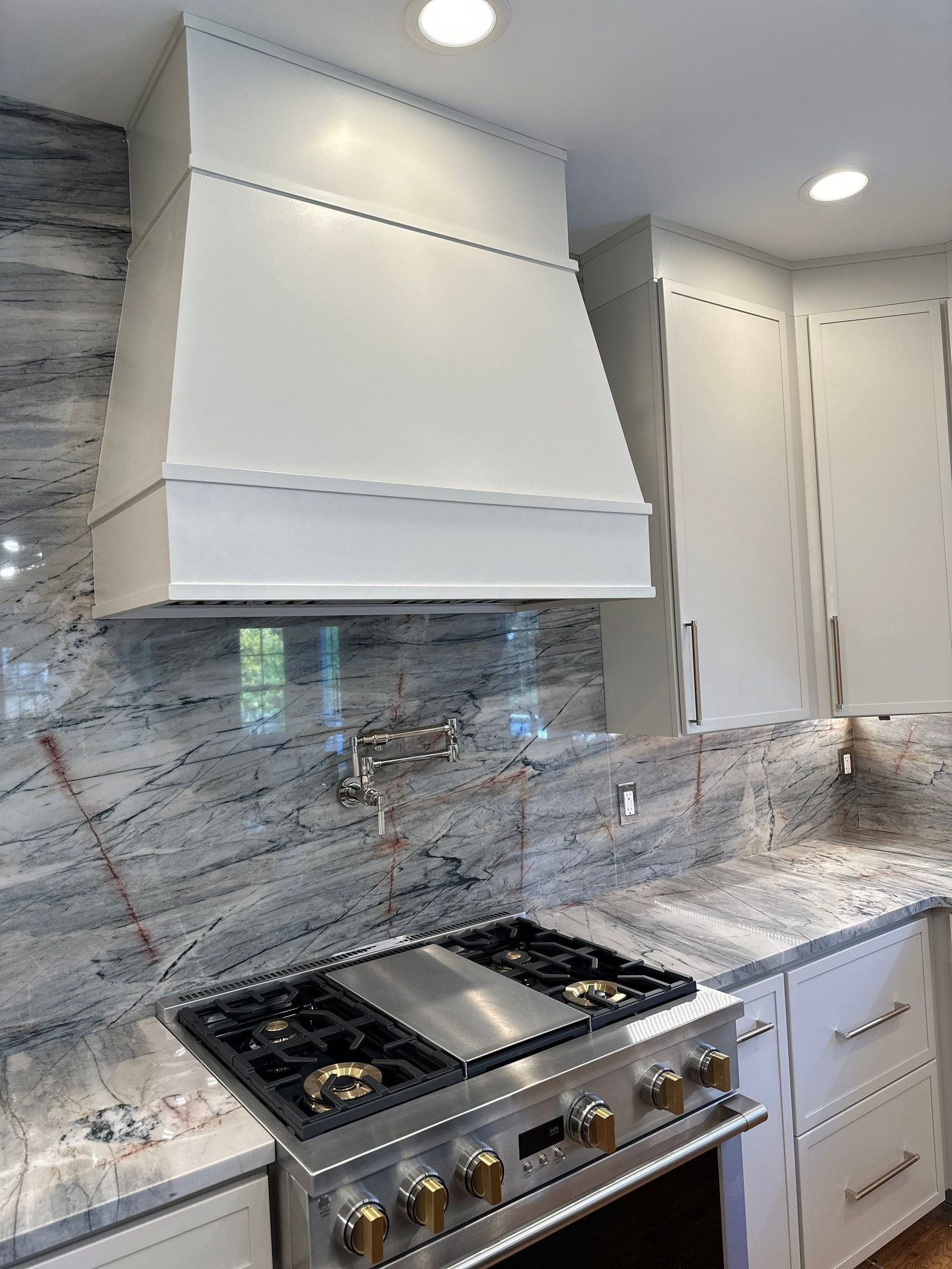 Westfield kitchen renovation featuring white shaker cabinets, gray veined marble backsplash and countertops, stainless steel gas range with griddle, white box hood, recessed ceiling lights, and brushed nickel hardware.
